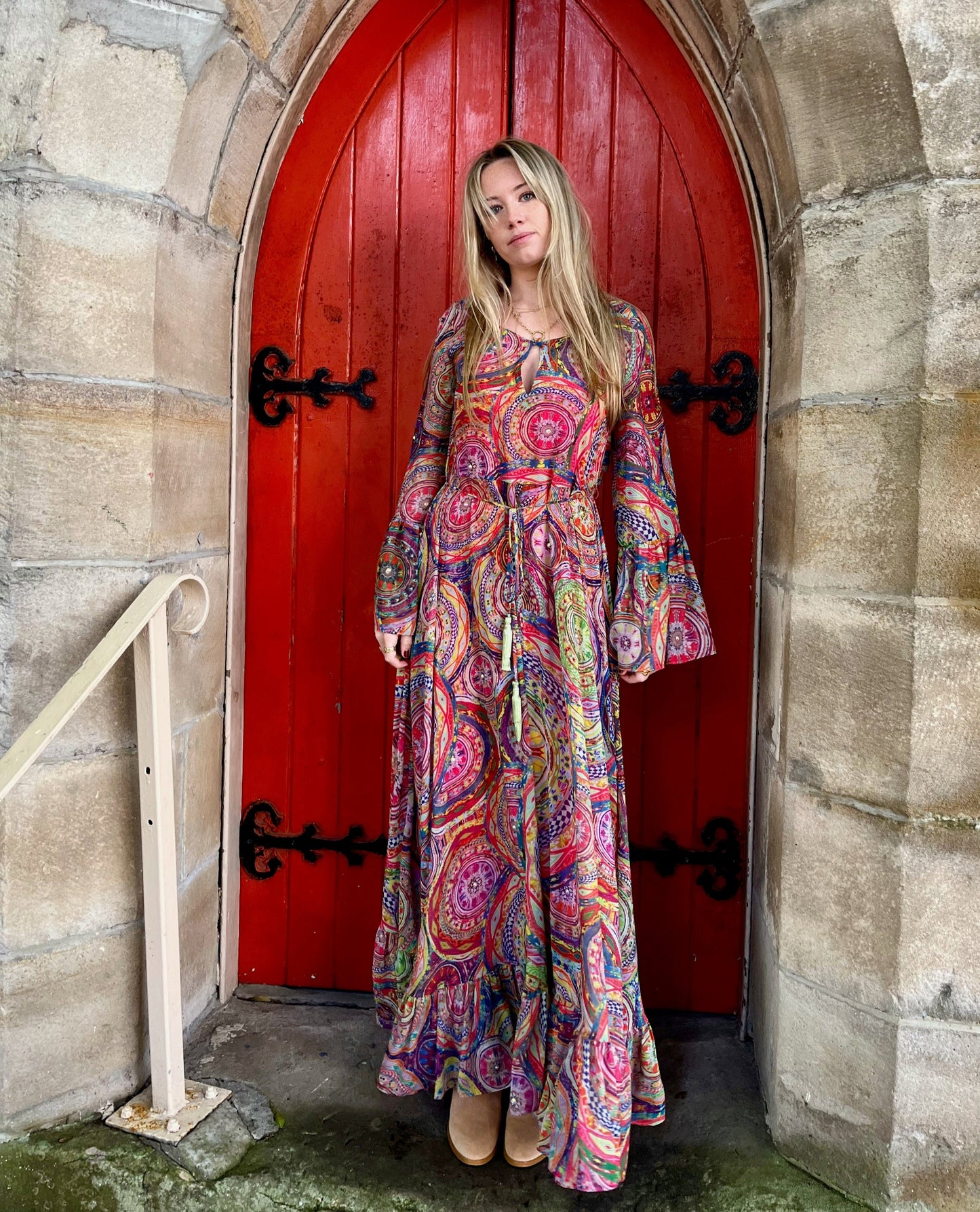 Woman in a colorful dress standing in front of a red door with stone archway