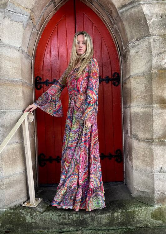 Woman in a colorful dress standing in front of a red door on a stone wall.