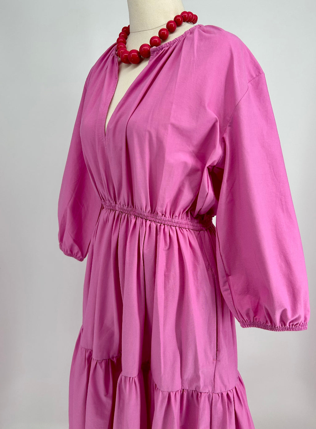Pink dress on a mannequin with a red necklace against a white background