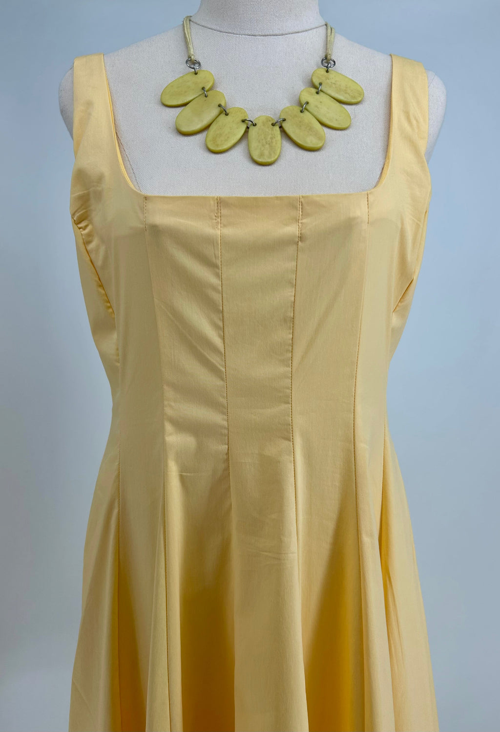 Yellow dress on a mannequin with a necklace against a gray background