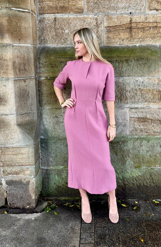 Woman in a pink  Emilia Wickstead dress standing against a stone wall.
