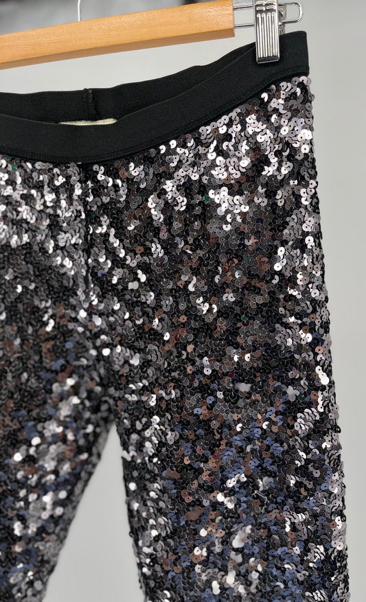 silver sequin pants on a hanger against a gray background