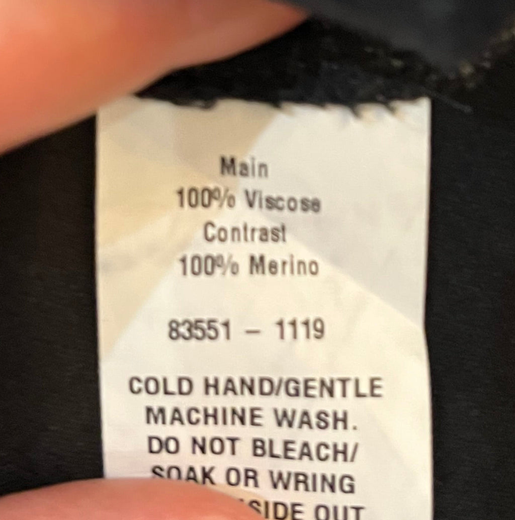 Clothing label on a black garment with text and a hand holding it.