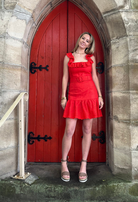 Woman in a red dress standing in front of a red door with stone archway