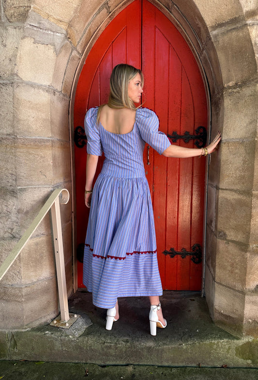 Woman in a blue dress standing on a stone ledge with a red door in the background