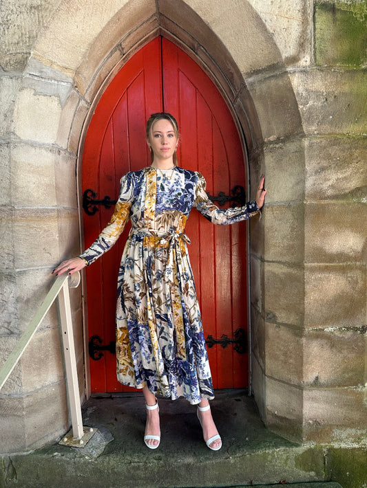Woman in a floral dress standing in front of a red door with stone walls.