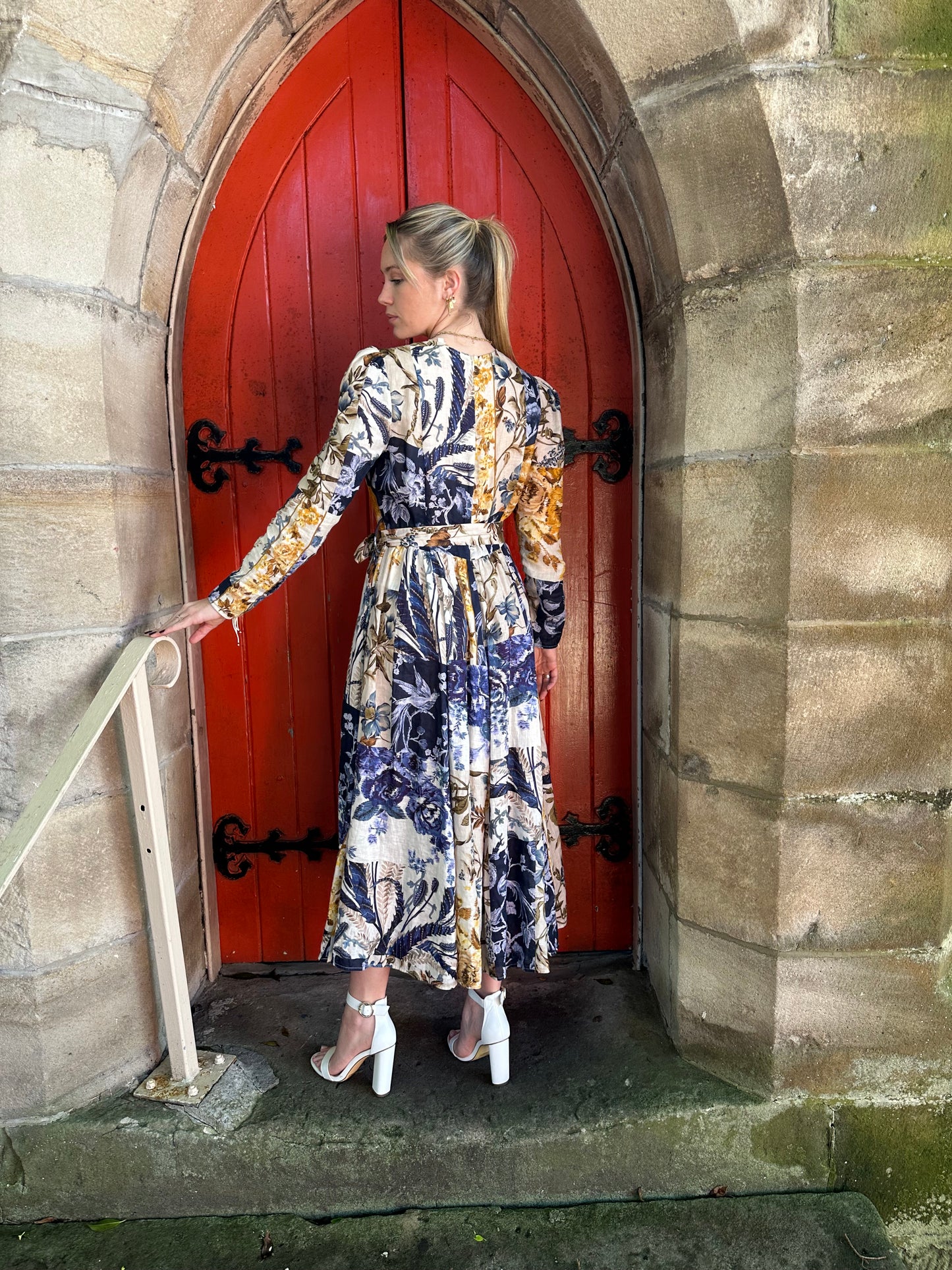 Woman in a floral dress standing on a ladder against a red door.