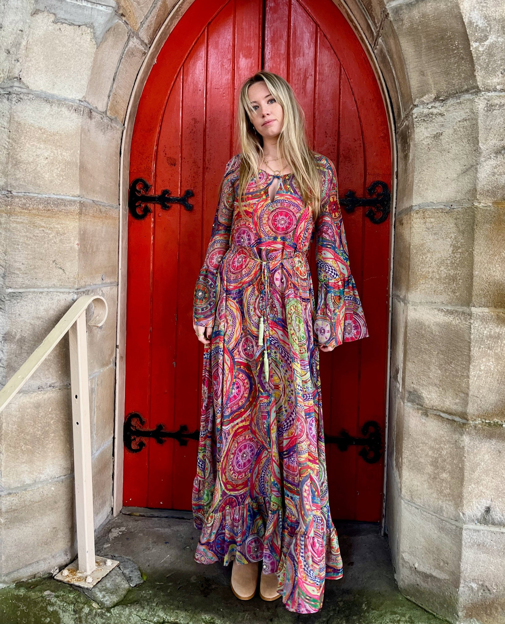 Woman in a colorful dress standing in front of a red door with stone archway