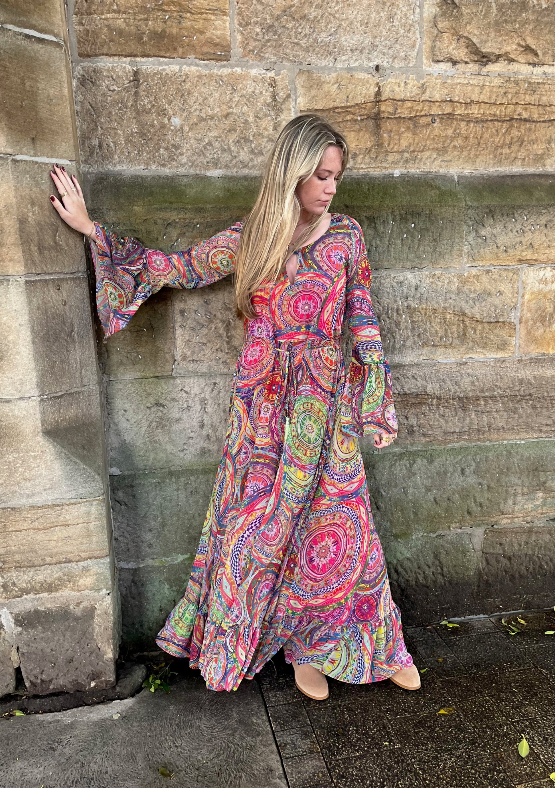 Woman in a colorful dress leaning against a stone wall.