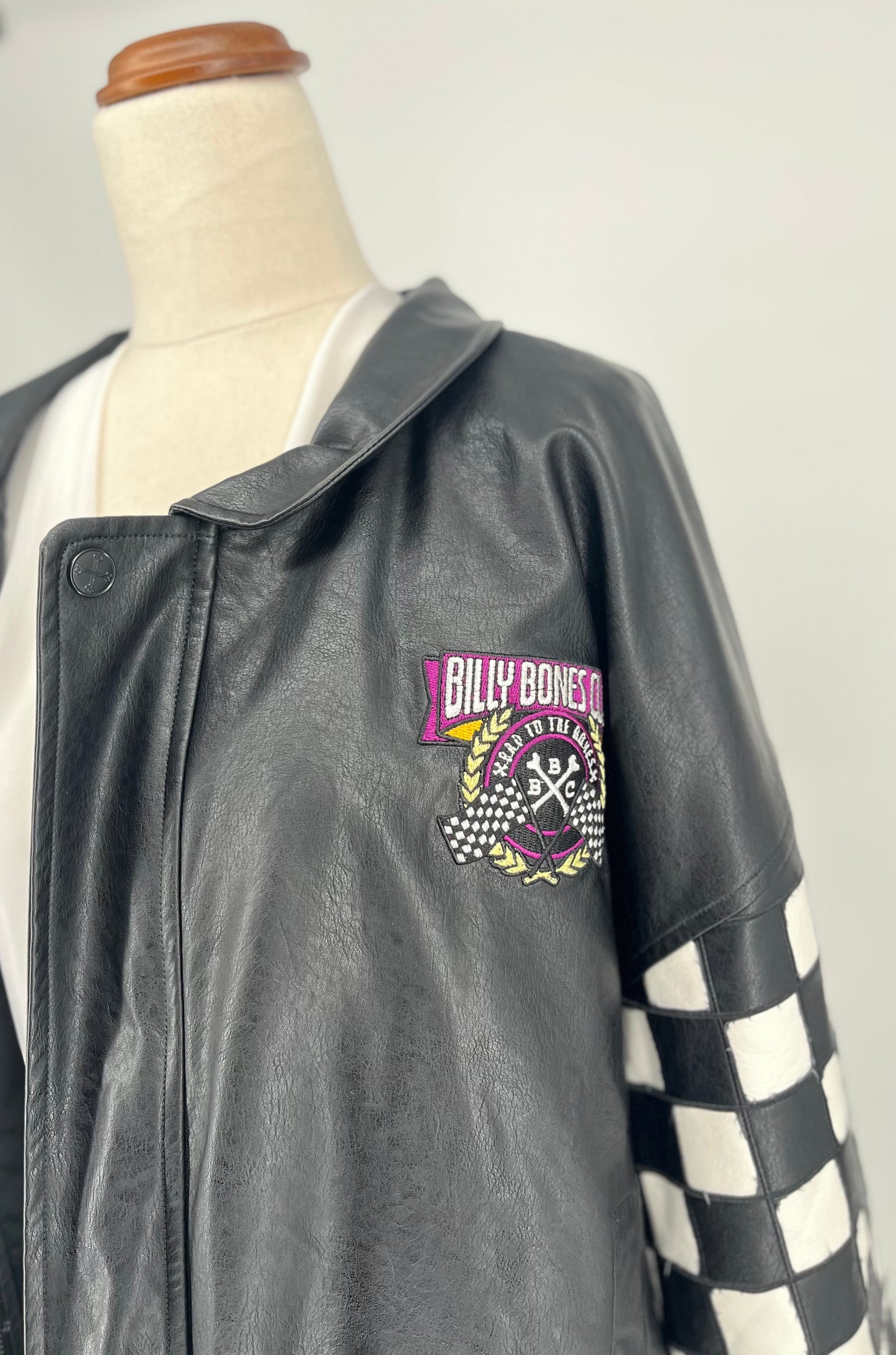 Gray leather jacket with checkered sleeves on a mannequin against a white background