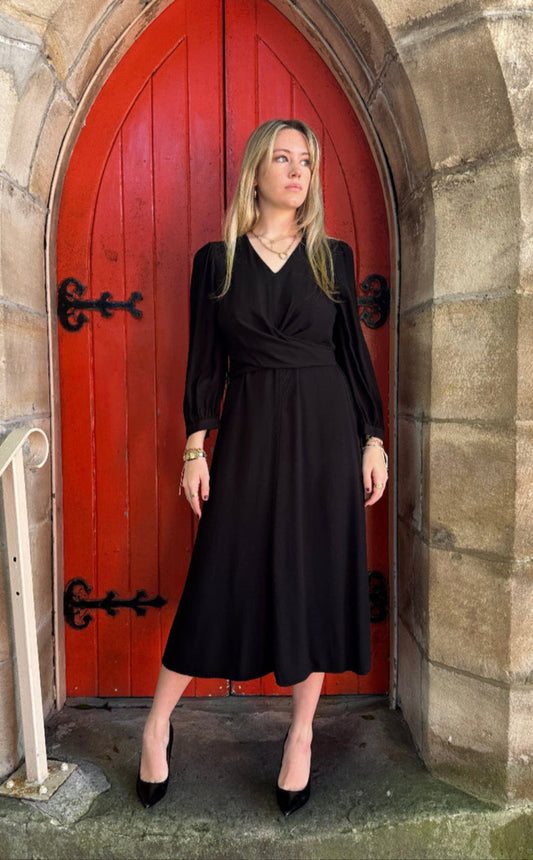 Woman in a black dress standing inside a red door with a stone wall background