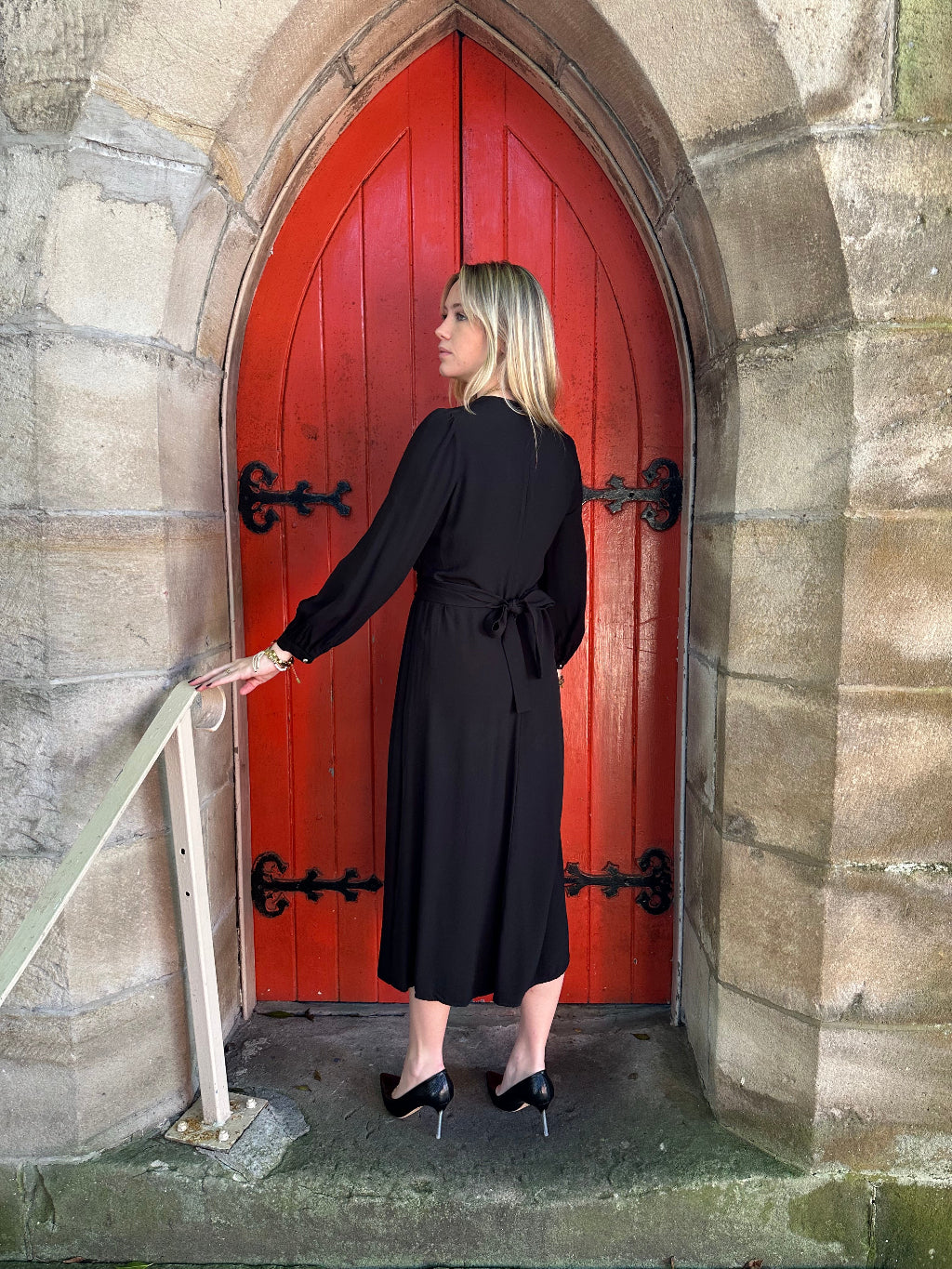 Woman in a black dress standing on a red door with stone walls and floor.