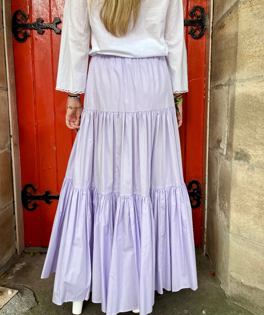 Person wearing a white blouse and long purple skirt standing in front of a red door.
