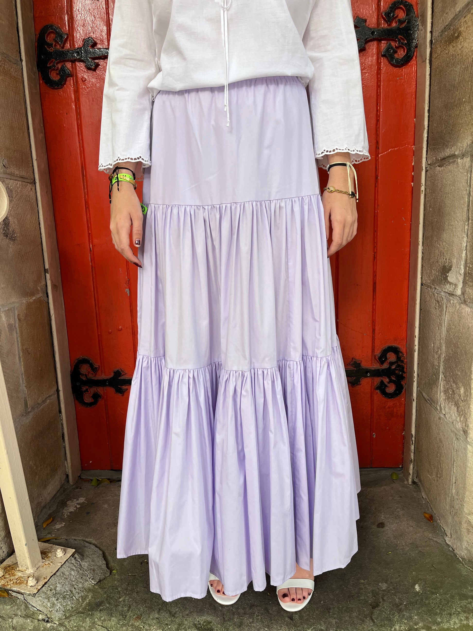 Person wearing a white dress with pleated skirt in front of a red door.