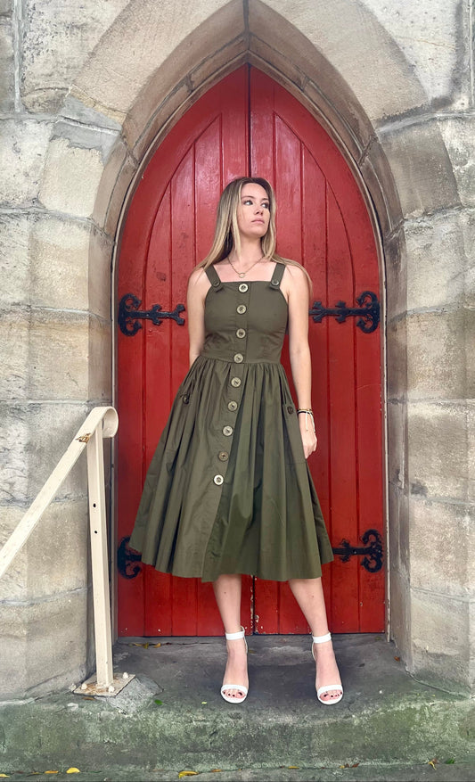 Woman in a green dress standing in front of a red door on a stone wall.