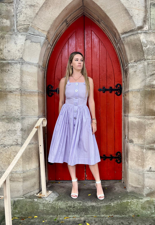 Woman in a purple dress standing in front of a red door on a stone wall.
