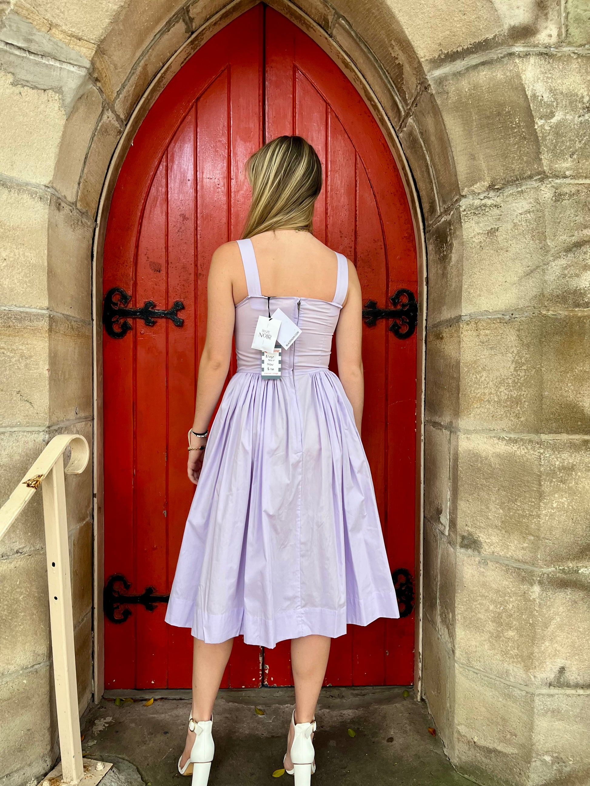 Woman in a purple dress standing in front of a red door.