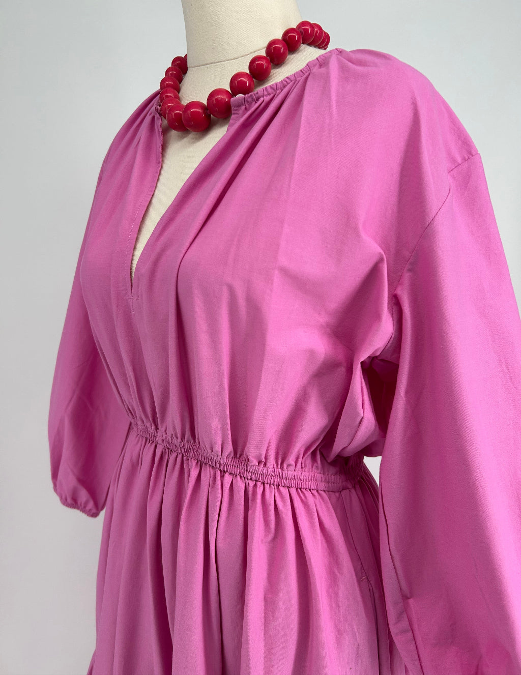 Close-up of a pink garment on a mannequin with a red beaded accessory.