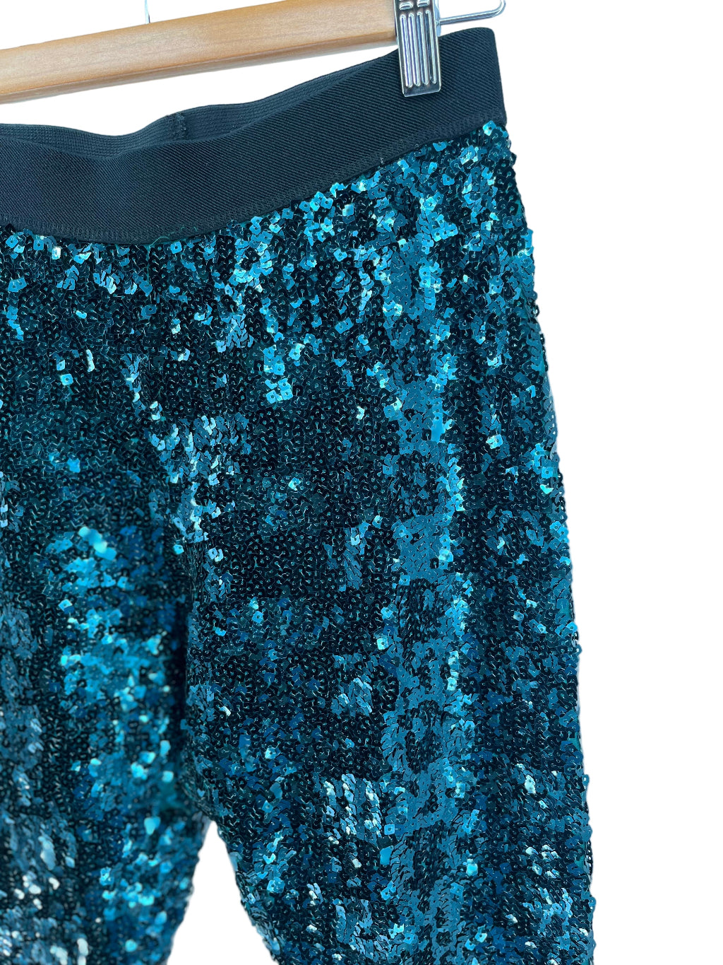 Close-up of blue sequin pants on a hanger against a white background