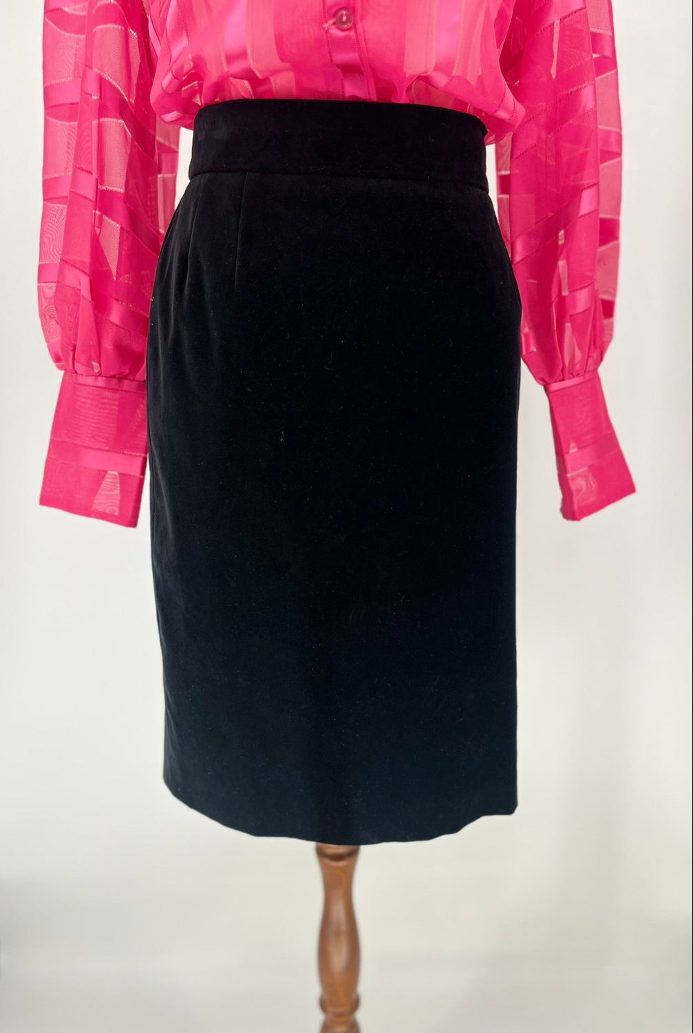 Black skirt on a mannequin with a pink sheer blouse in the background