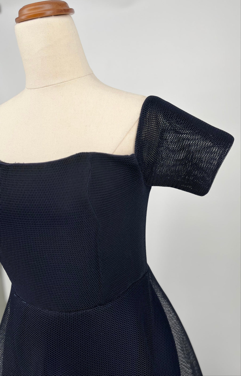 Black dress on a mannequin with a textured shoulder detail against a plain background