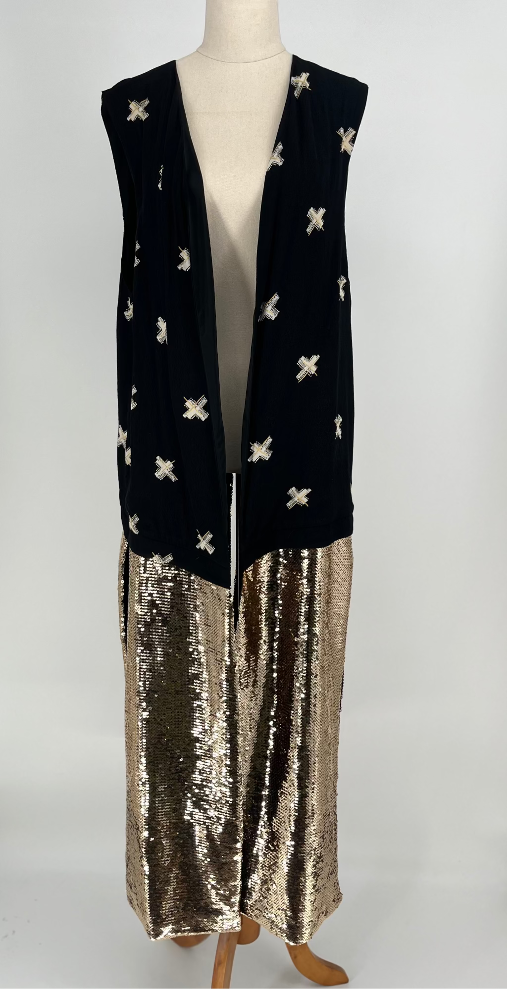 Black vest with white patterns and gold sequin trim on a mannequin against a white background