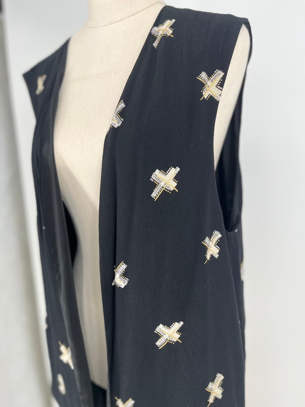 Black sleeveless top with white cross patterns on a mannequin against a white background