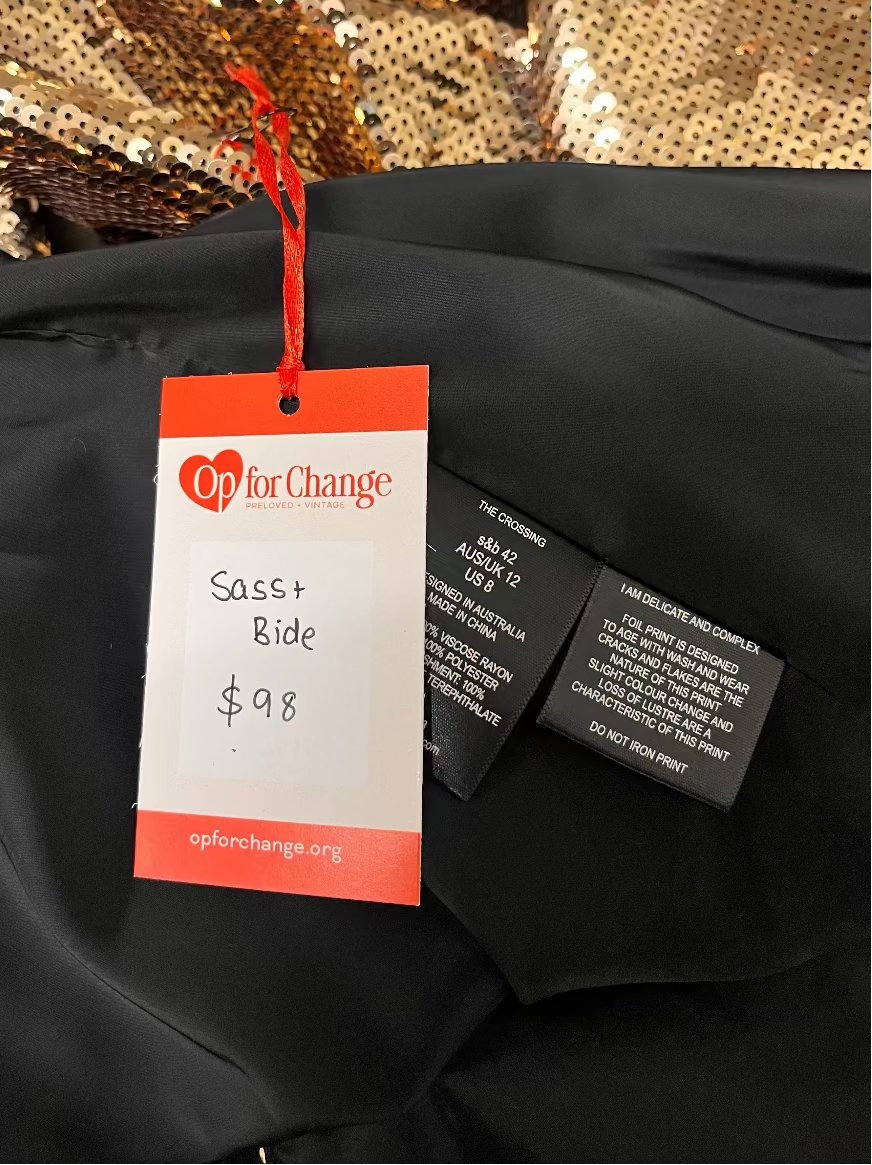 Black jacket with a 'Op for Change' tag and gold sequin fabric in the background