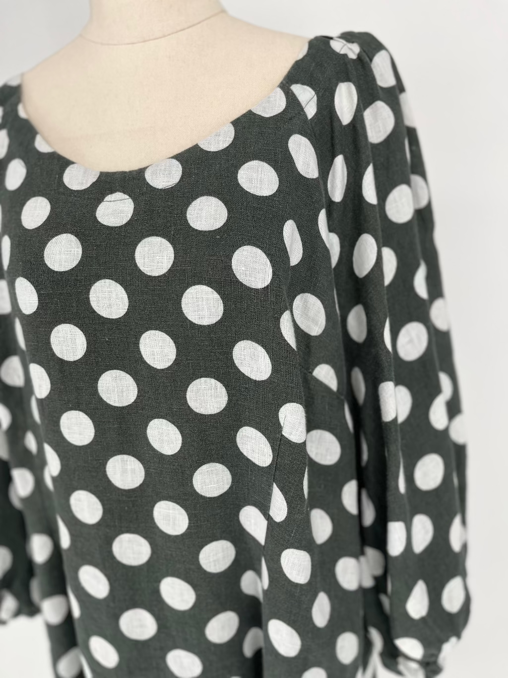 Olive dress with white polka dots on a mannequin against a white background