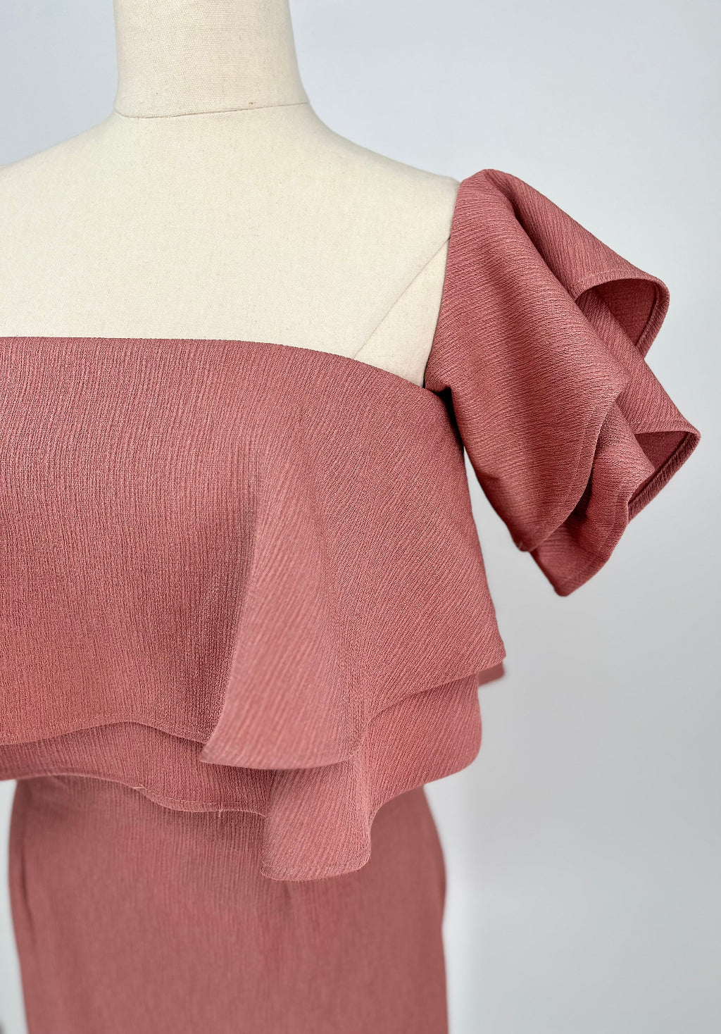 Pink ruffled top on a mannequin against a white background