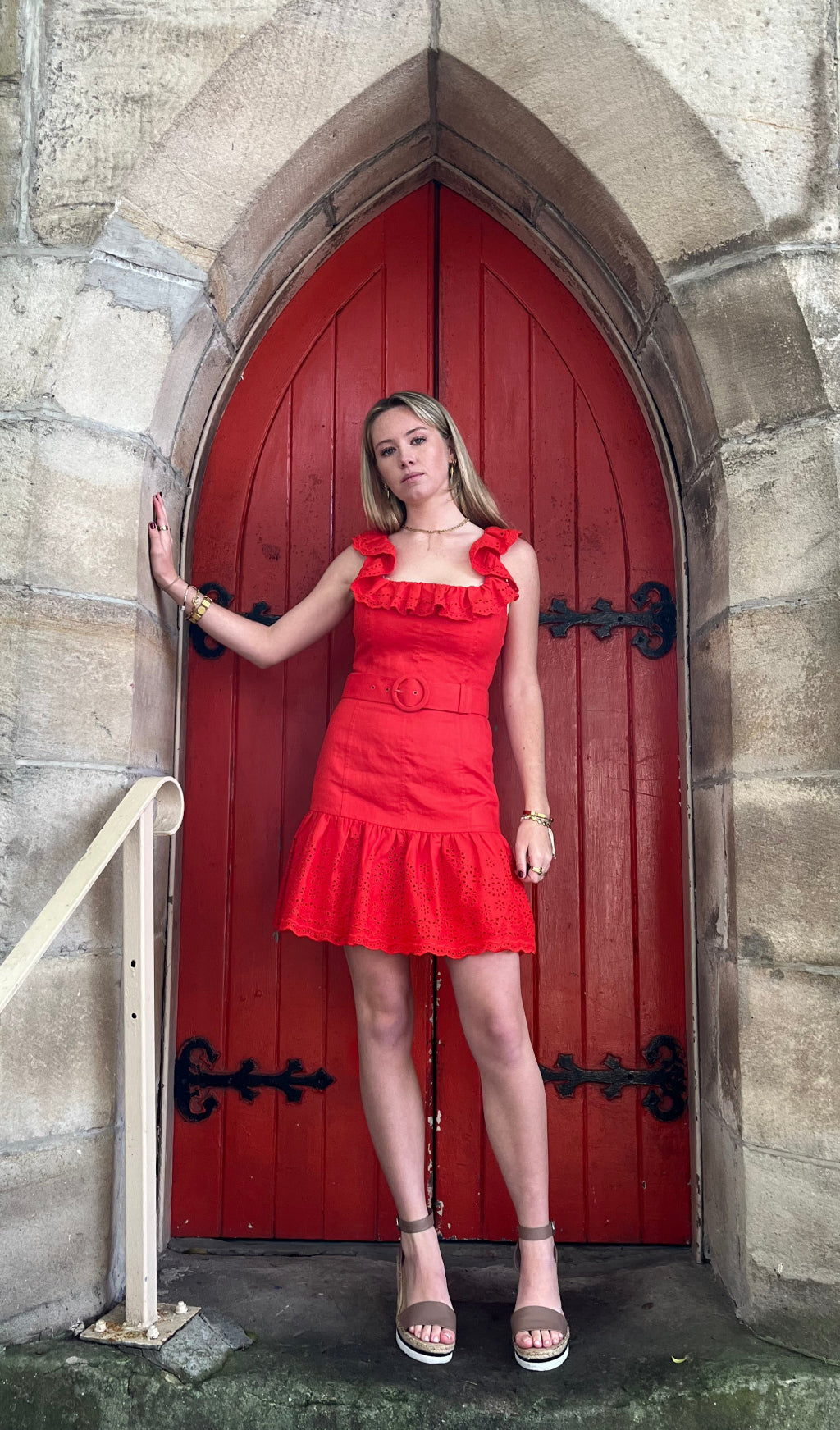 Woman in a red dress lying on a red door set into a stone wall.