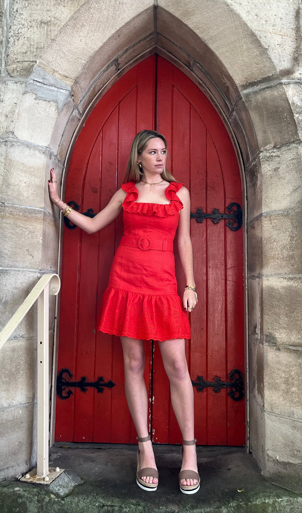 Woman in a red dress standing in a stone archway with a red door.