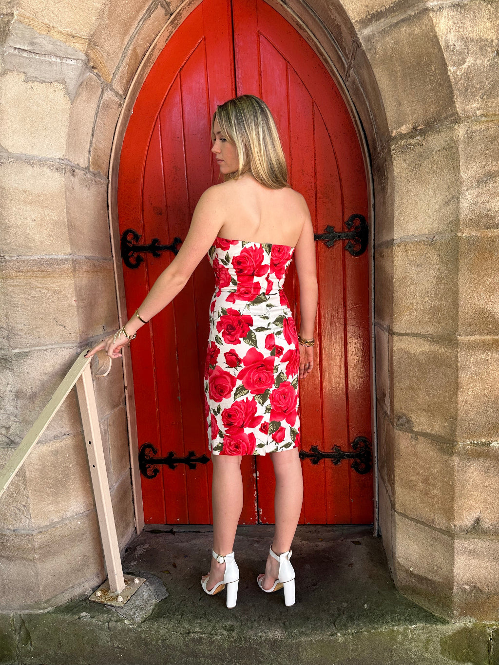 Woman in a floral dress standing on a wooden door with a stone wall background