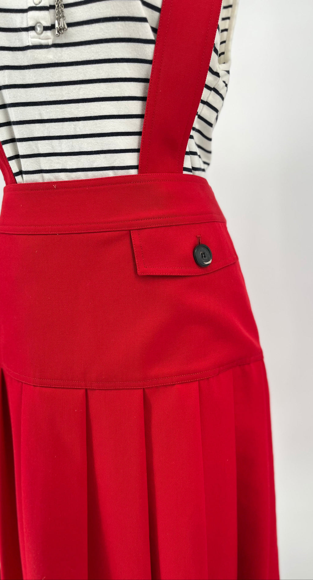 Red pinafore dress over a striped shirt on a plain background