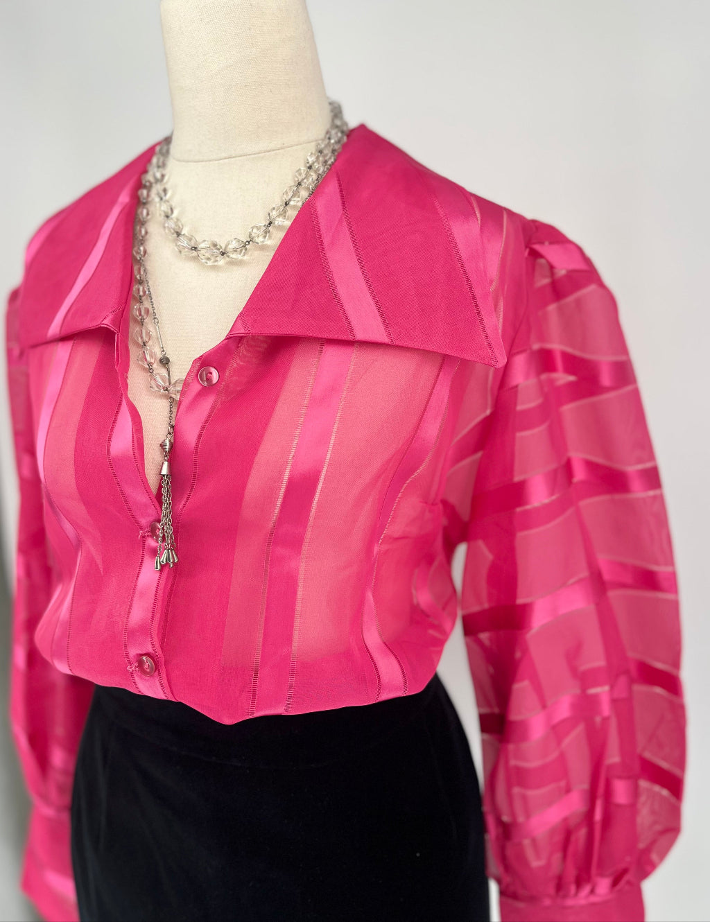 Pink sheer blouse on a mannequin with a white background