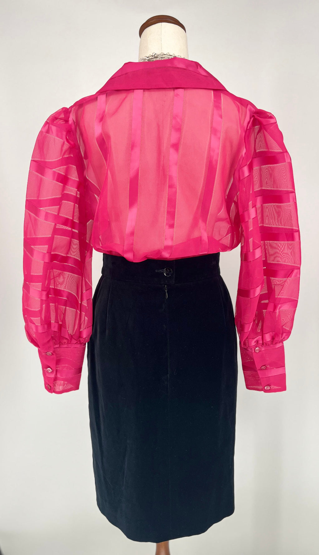 Mannequin wearing a pink sheer blouse over a black skirt on a white background