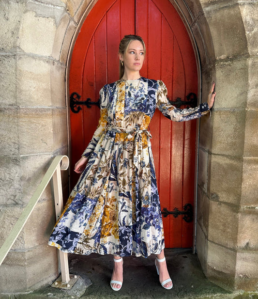 Woman in a floral dress standing in front of a red door with stone walls.