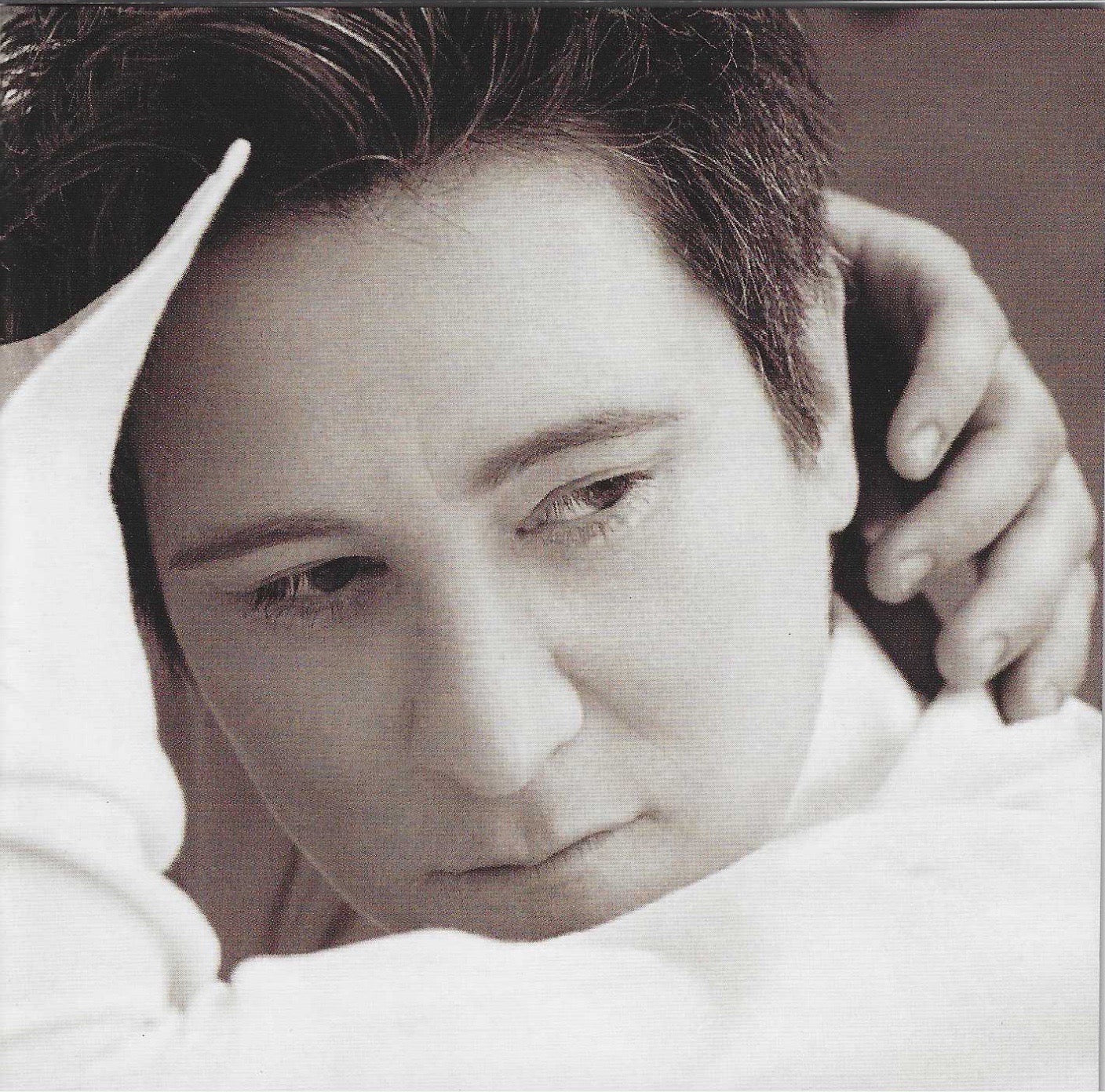 CD album cover of Watershed by k.d. lang. Photo shows black and white close-up of lang with a hand on their head, wearing a white garment.